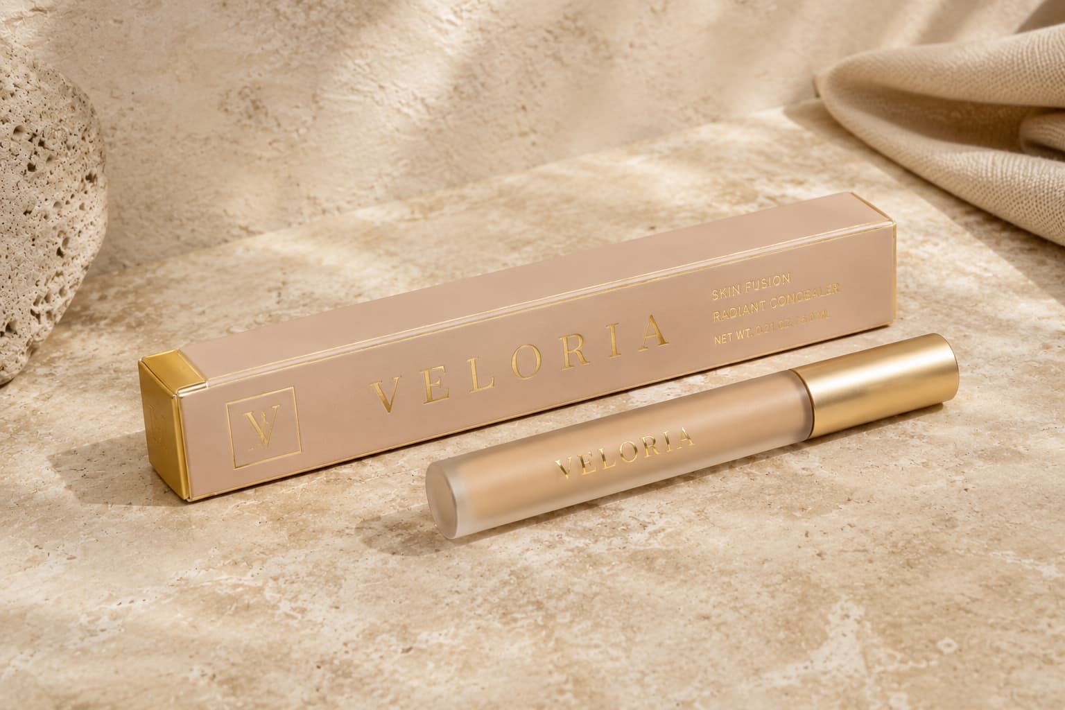 Elegant concealer box and tube in soft beige packaging with gold foil branding on a textured stone background