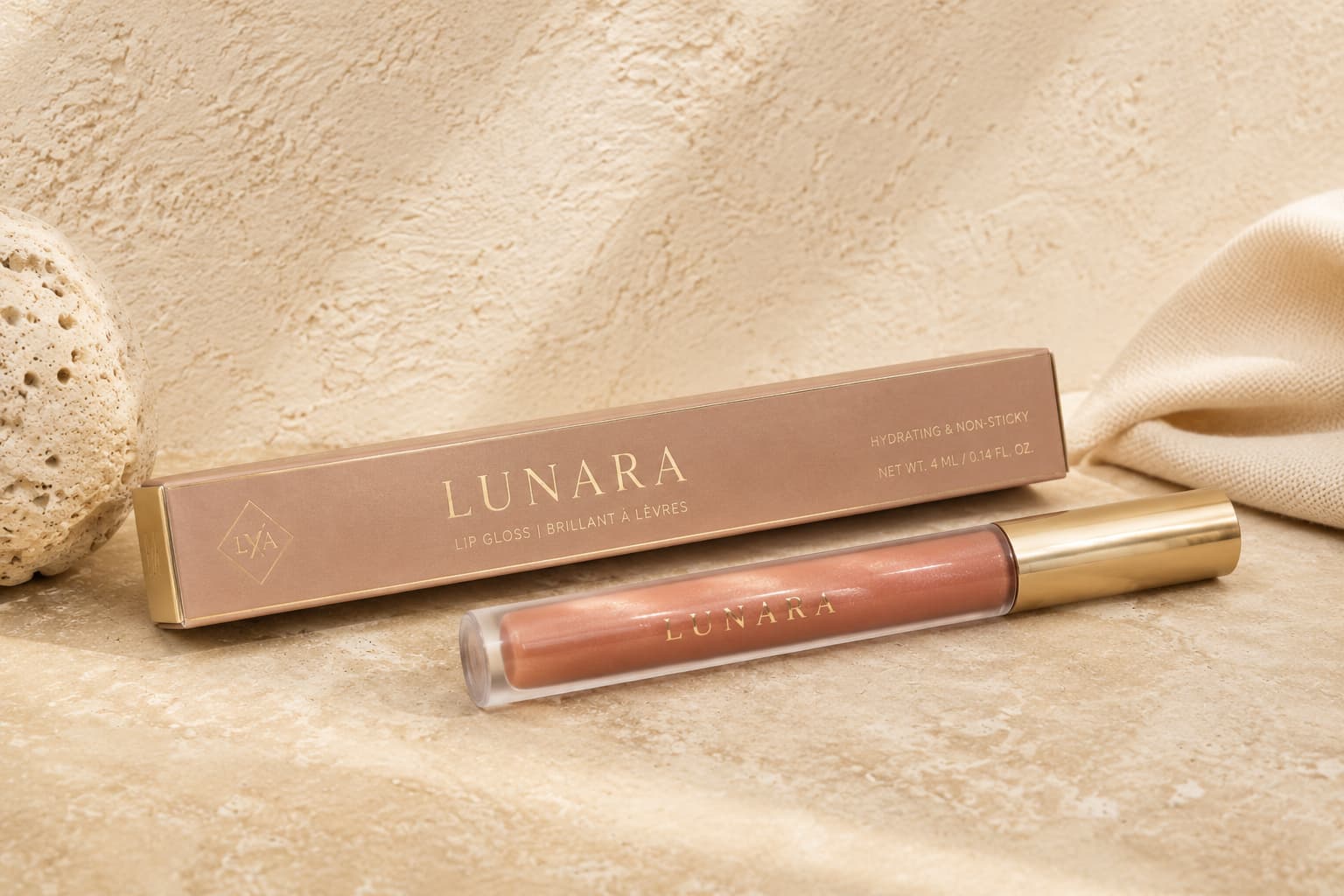 Luxury lip gloss box and tube in nude pink packaging with gold foil details on a textured beige surface